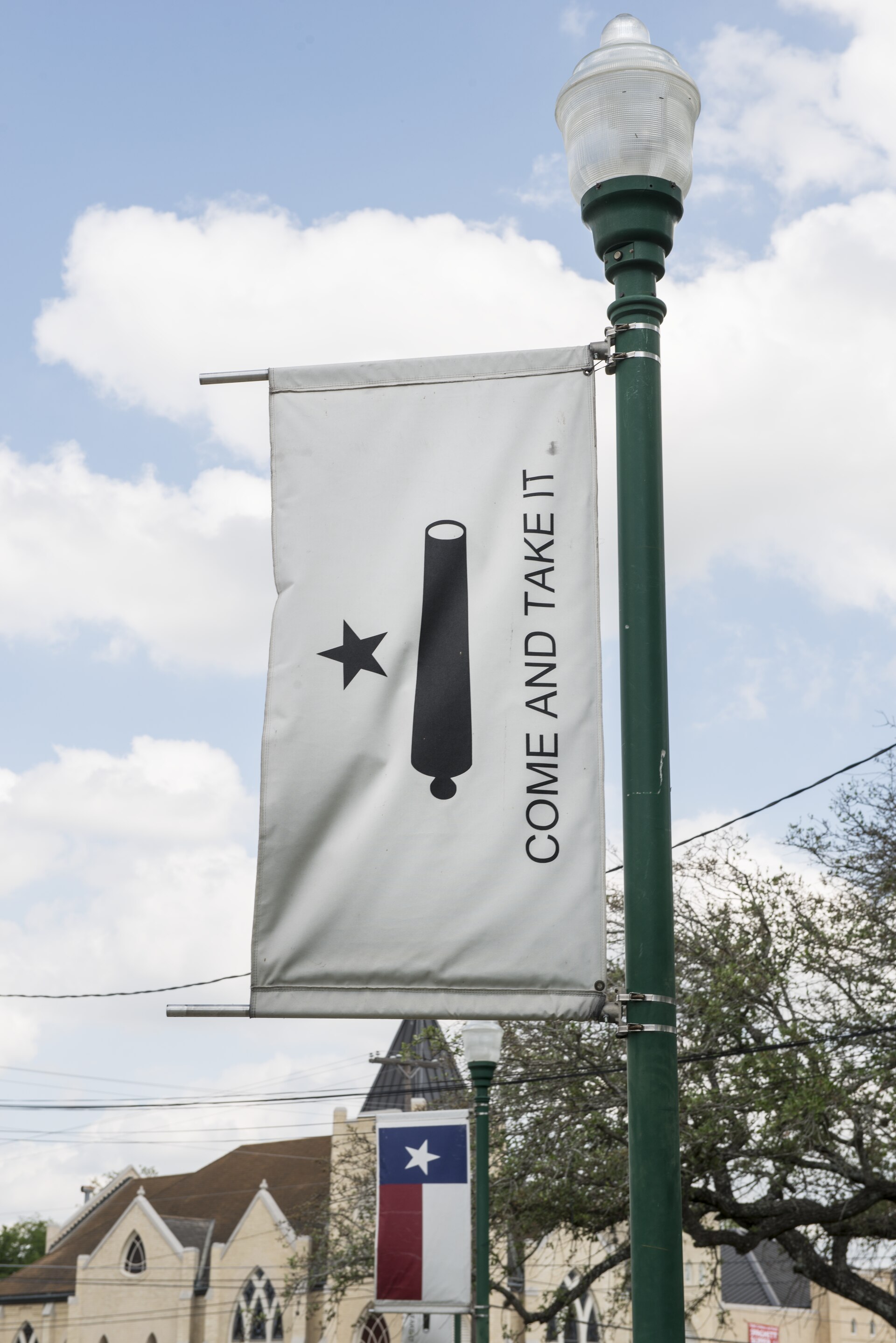 A white banner with a black star, a black cannon and the words Come and Take It hangs from a lamppost in Gonzales